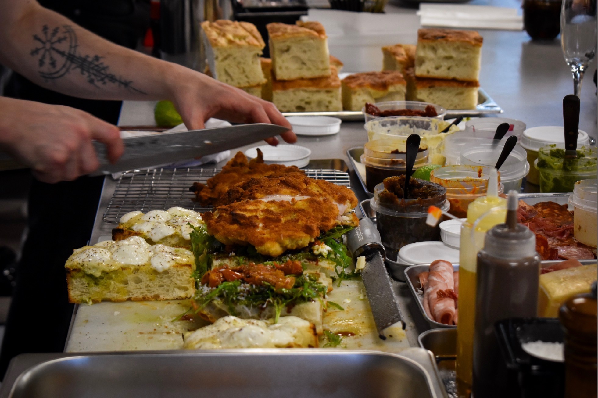 A chef preparing focaccia sandwiches at the Ruger Fjord counter with fresh bread, fillings and sauces laid out.