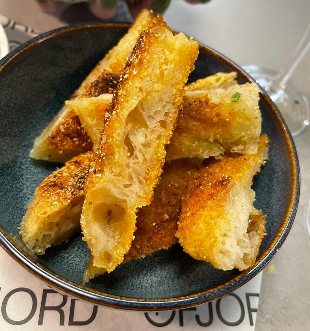 A bowl of Ruger Fjord Pocaccia: pan-fried, puffed panko focaccia fingers with a golden crisp crust and light, open crumb, served on branded Fjord paper.