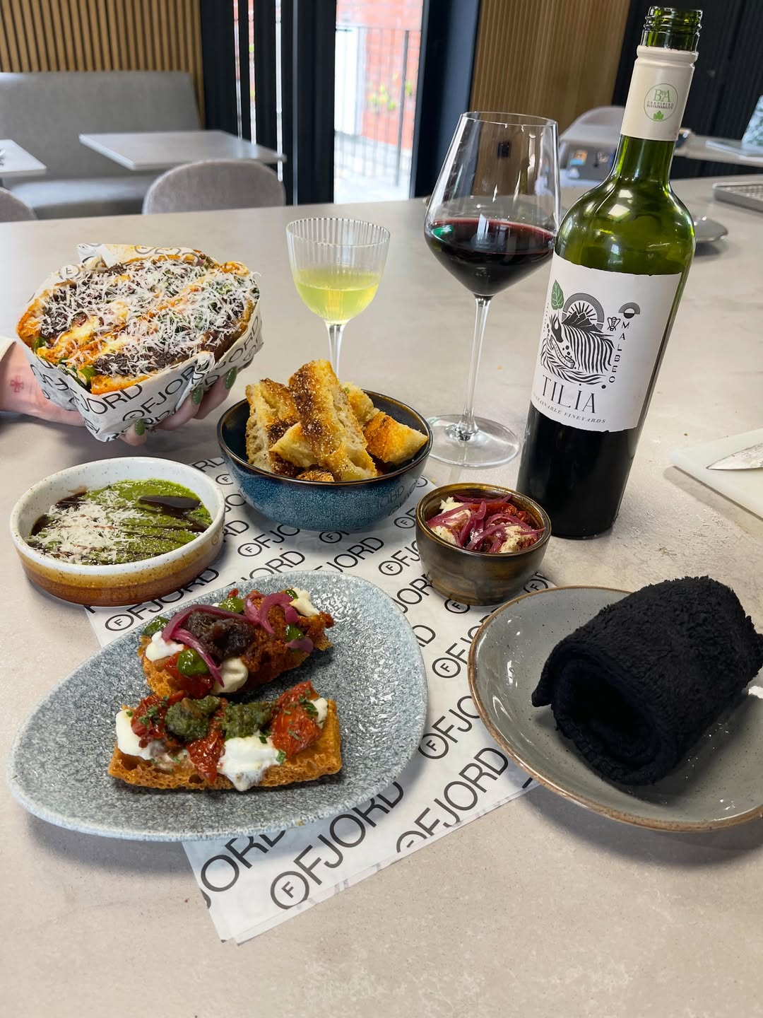 A Ruger Fjord table experience spread on branded paper: focaccia bites, dips, charcuterie and glasses of red and white wine.