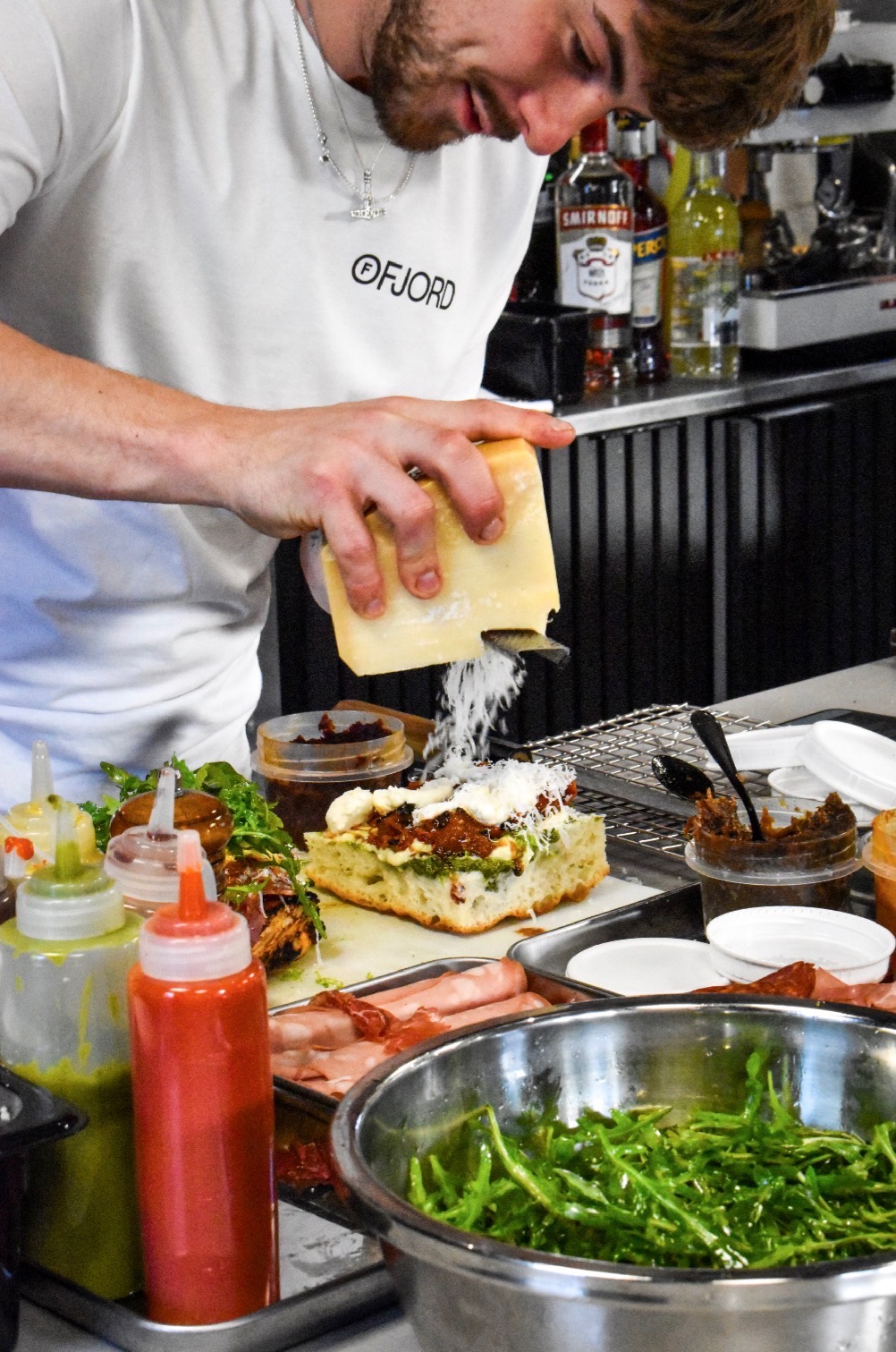 A Ruger Fjord chef grating hard cheese over a freshly built focaccia at the prep station.